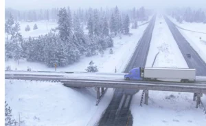 A blue semi-truck equipped with ISAAC's durable trucking technology solutions crossing a snowy bridge, showcasing system reliability in harsh weather conditions.