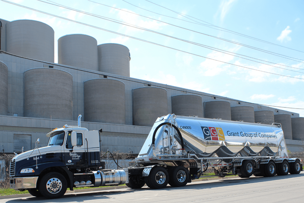 Camion semi-remorque de Grant Group of Companies garé devant de grands silos industriels sous un ciel bleu.