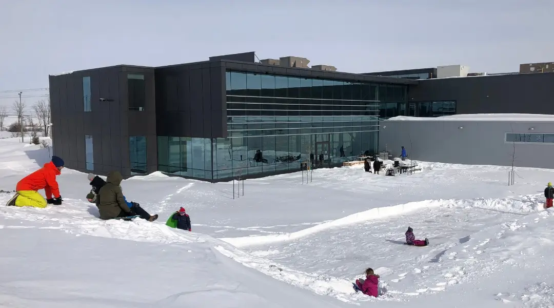 Employees and families sledding on a snowy hill in front of the ISAAC Instruments headquarters