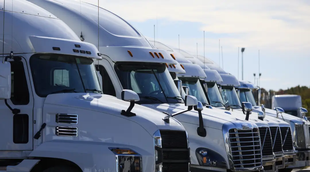 A lineup of white semi-trucks parked in a row, showcasing advanced trucking technology.